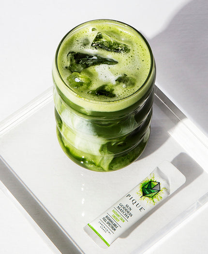 Glass of iced matcha beverage beside a packet of Pique Sun Goddess Matcha.