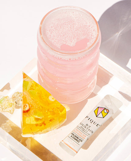 Pink drink on a table beside sliced translucent yellow jelly and a packet labeled 'Pique BT Fountain Beauty Electrolytes.'